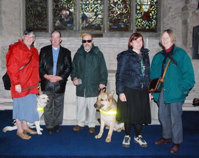From left to right are Denise Collier with her Guide Dog Honey, Terry Collier, Eric Sayce with his Guide Dog Wills, Bella Murdoch and Julia Ionides. They are standing in front of the Jesse Window in the Lady Chapel.